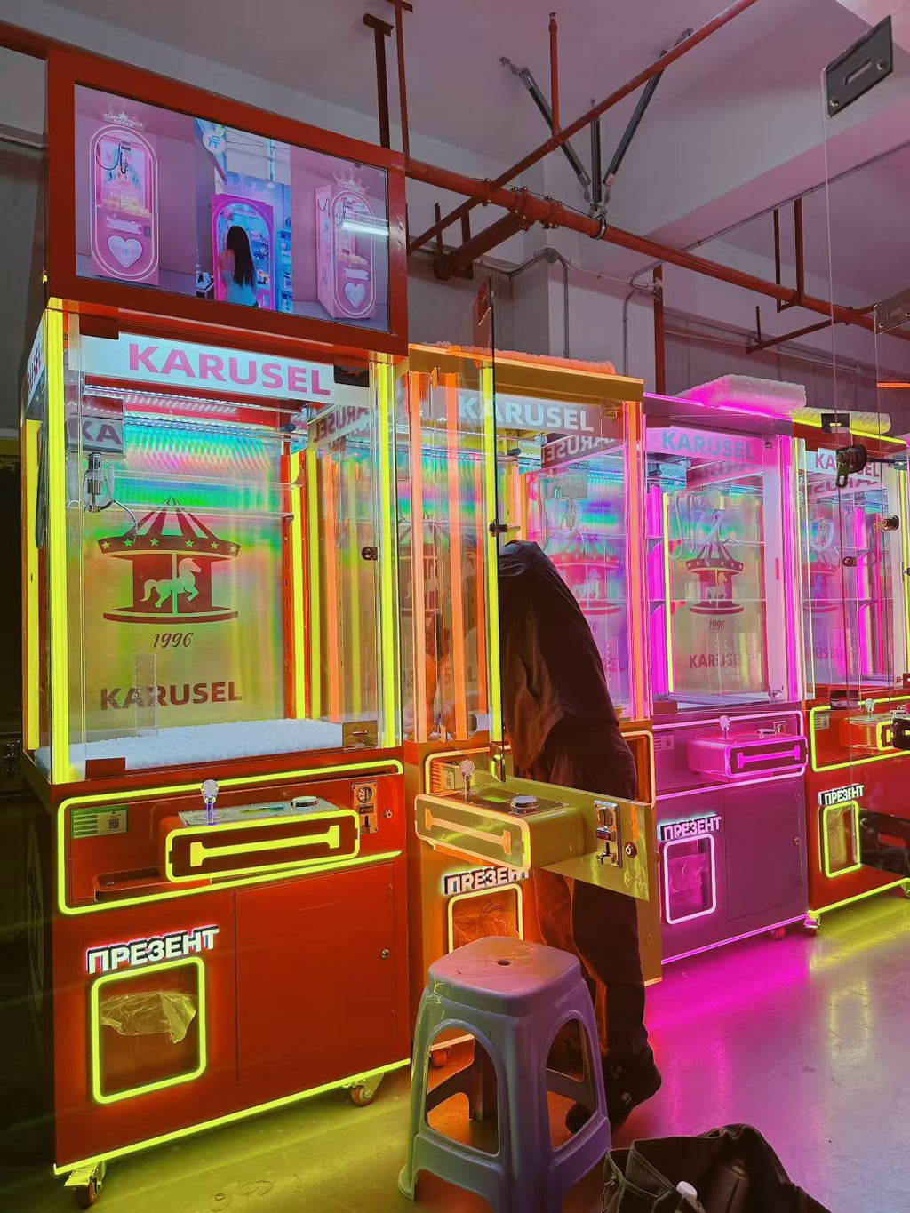 Video game arcade with doll catching machines featuring advertising screens and holding figurines for games and gift dispensers