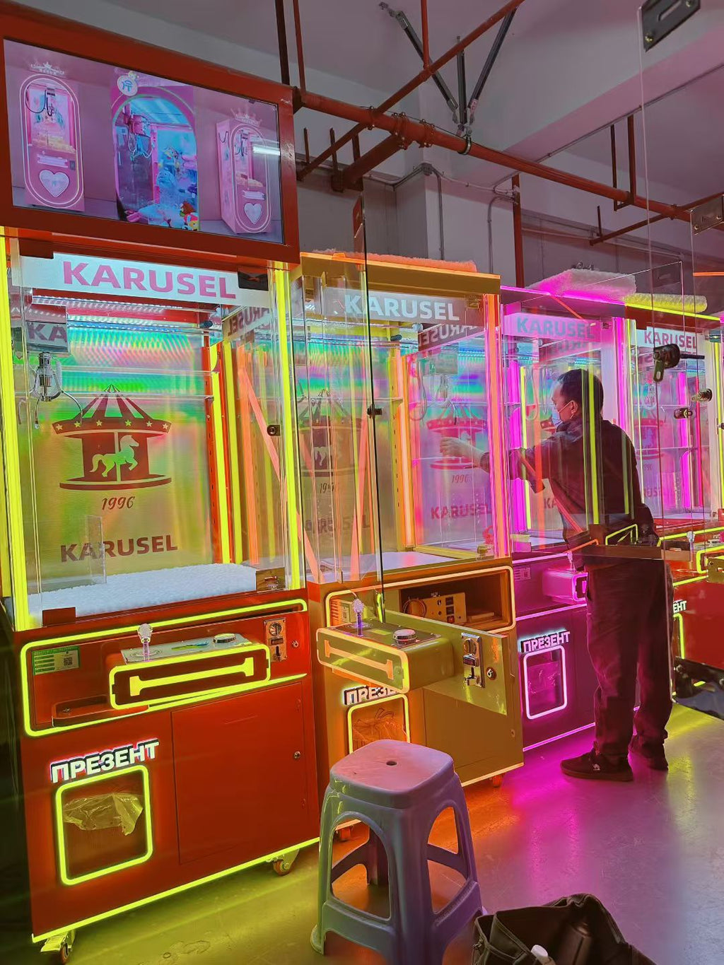 Video game arcade with doll catching machines featuring advertising screens and holding figurines for games and gift dispensers