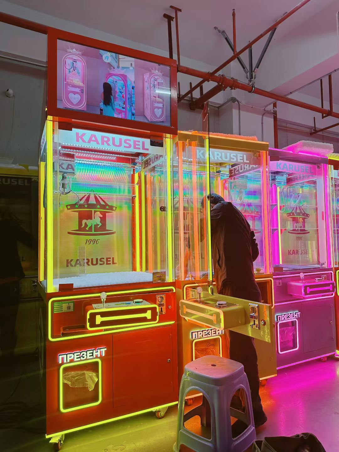 Video game arcade with doll catching machines featuring advertising screens and holding figurines for games and gift dispensers